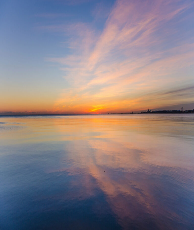 A calm ocean at sunset with soft light reflecting on the water.