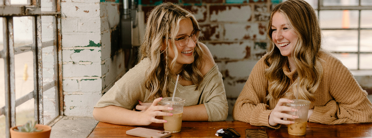 Two people sharing a quiet conversation over coffee in warm natural light, reflecting human connection and kindness in everyday life.