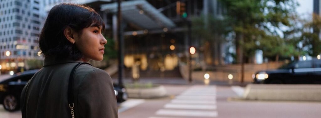 A woman quietly waits at a crosswalk, reminding us that every person we pass is carrying a story we cannot see.